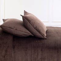 Two brown corduroy pillows resting on a matching brown corduroy bedspread or sofa, set against a white paneled wall.