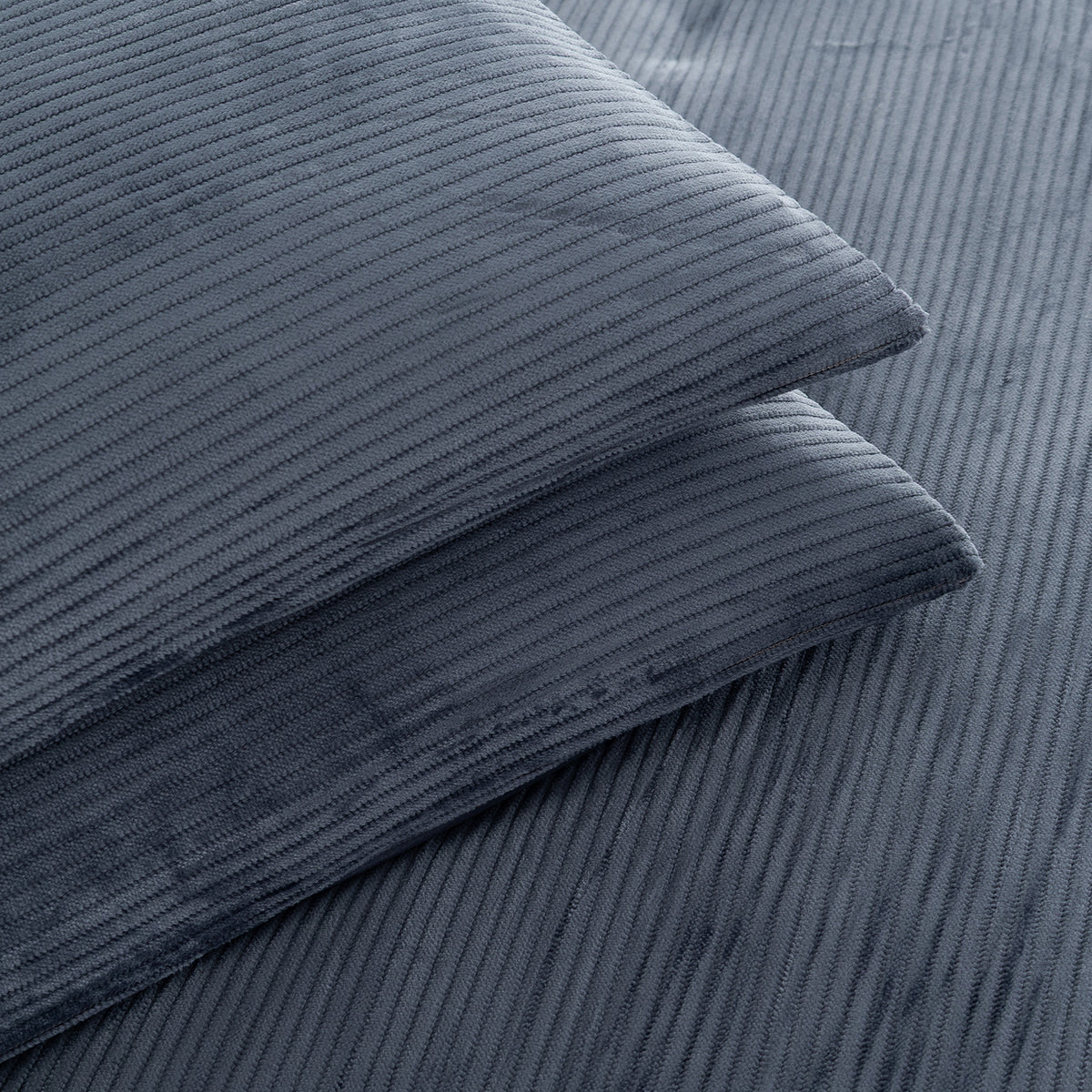 A close-up of two folded corduroy pillows in a slate blue-gray color, showcasing the ribbed texture of the fabric.