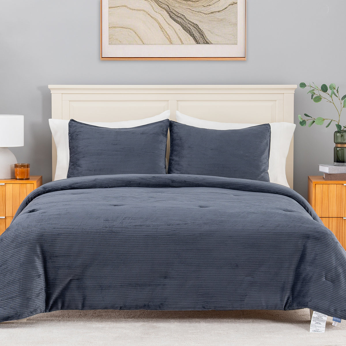 A navy blue corduroy comforter set with matching pillow shams on a bed, styled in a modern bedroom with a cream headboard, wooden nightstands, and a gray wall.