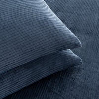 A close-up of a navy blue corduroy pillow resting on a matching navy blue corduroy fabric background.