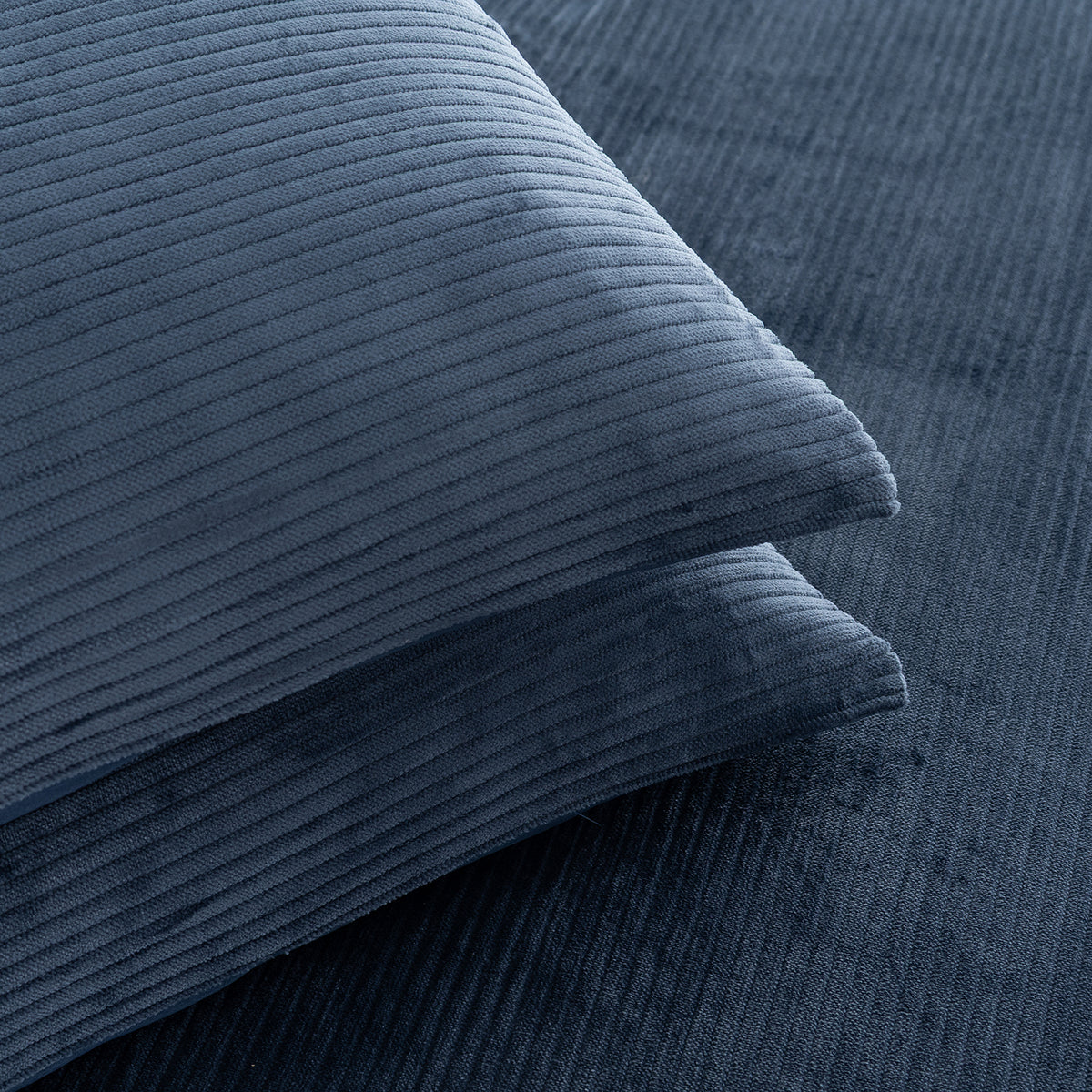 A close-up of a navy blue corduroy pillow resting on a matching navy blue corduroy fabric background.