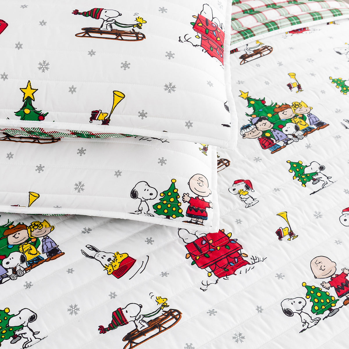 A close-up of a quilted bedding set featuring a white background with a colorful cartoon print of Peanuts characters, including Snoopy, Woodstock, Charlie Brown, and Peppyscrab. The set includes a comforter and matching pillowcases.