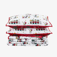 A stack of three white quilted bedding pieces with red trim and a festive Snoopy and Woodstock cartoon print, photographed on a light gray background.