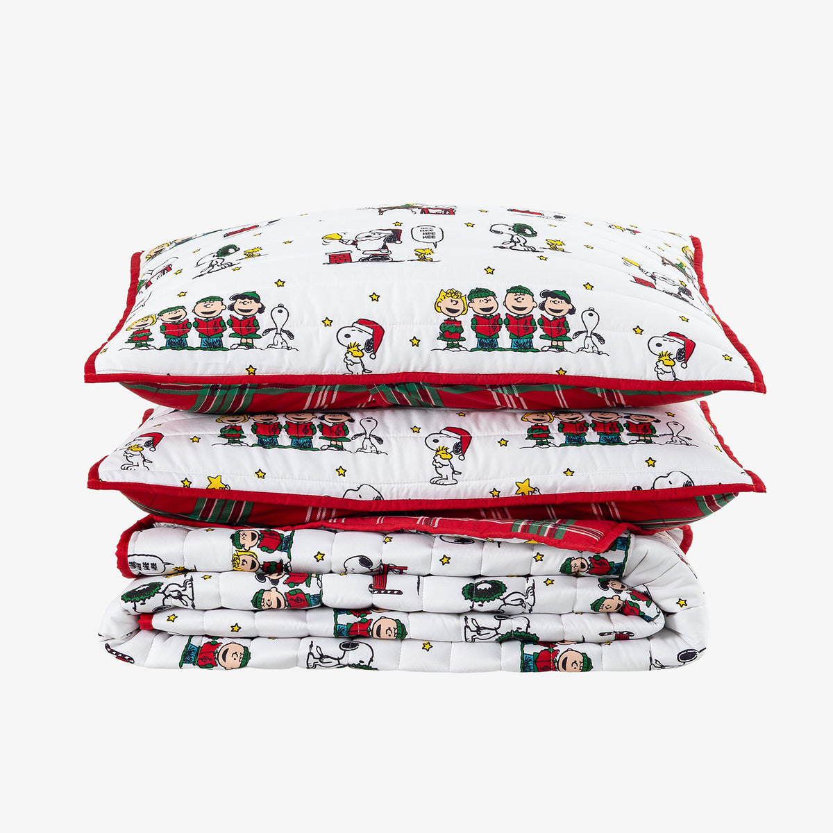 A stack of three white quilted bedding pieces with red trim and a festive Snoopy and Woodstock cartoon print, photographed on a light gray background.