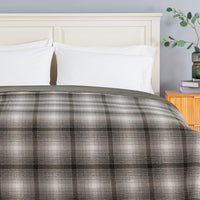 A plaid teddy fleece blanket dressed neatly on a bed in a bright bedroom.