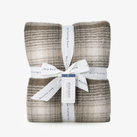 A plaid teddy fleece blanket folded neatly with a ribbon on a white surface.