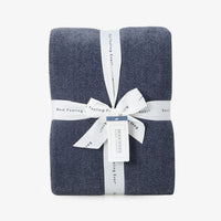 Dusty blue chenille knit blanket folded neatly with a ribbon on a white surface.