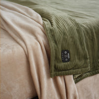VelvetLoft® Plush Sheet Set in Hummus with a green ribbed blanket and its controller laid across it
