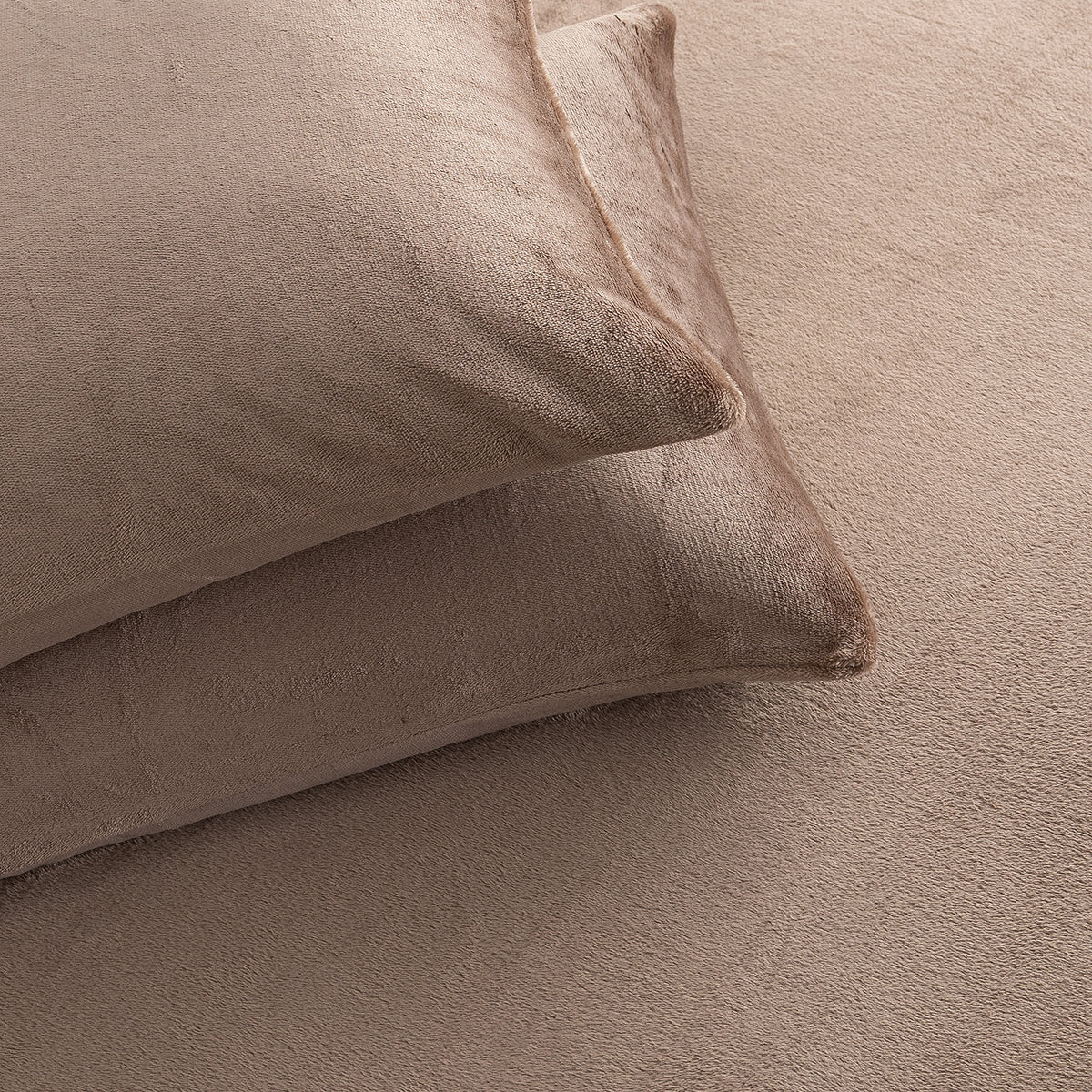 Two plush, textured beige pillows resting on a matching beige bedspread or blanket.