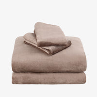 A stack of plush, folded bedding pieces in a warm taupe-brown color, set against a plain light gray background.
