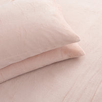 Two pale blush pink pillows resting on matching pink bedding with a soft, textured fabric surface.