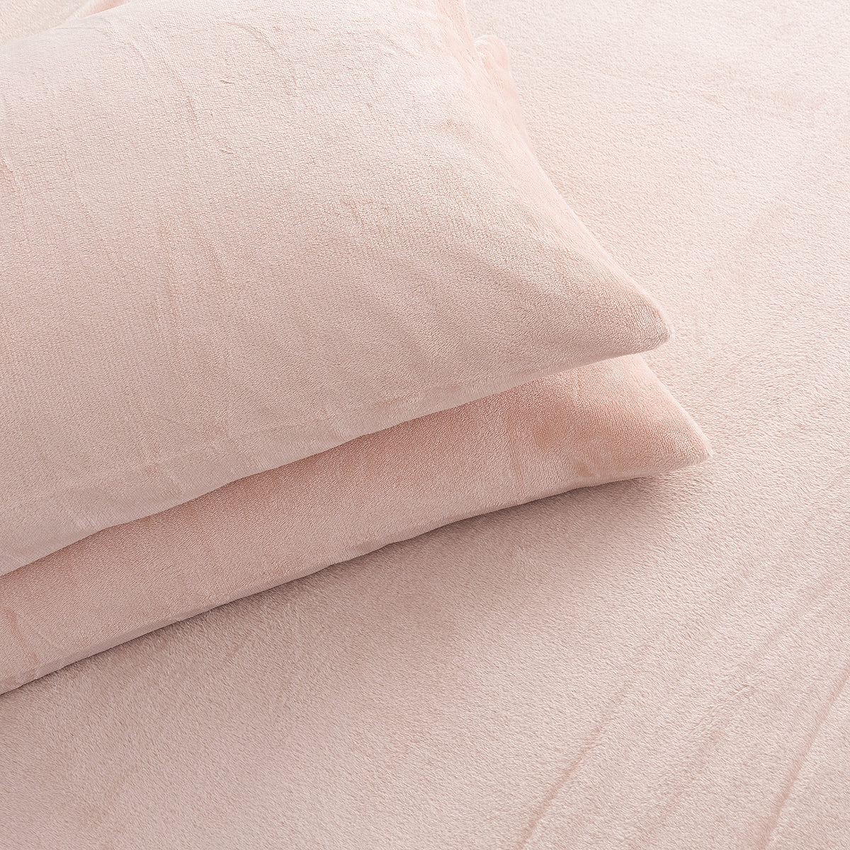 Two pale blush pink pillows resting on matching pink bedding with a soft, textured fabric surface.