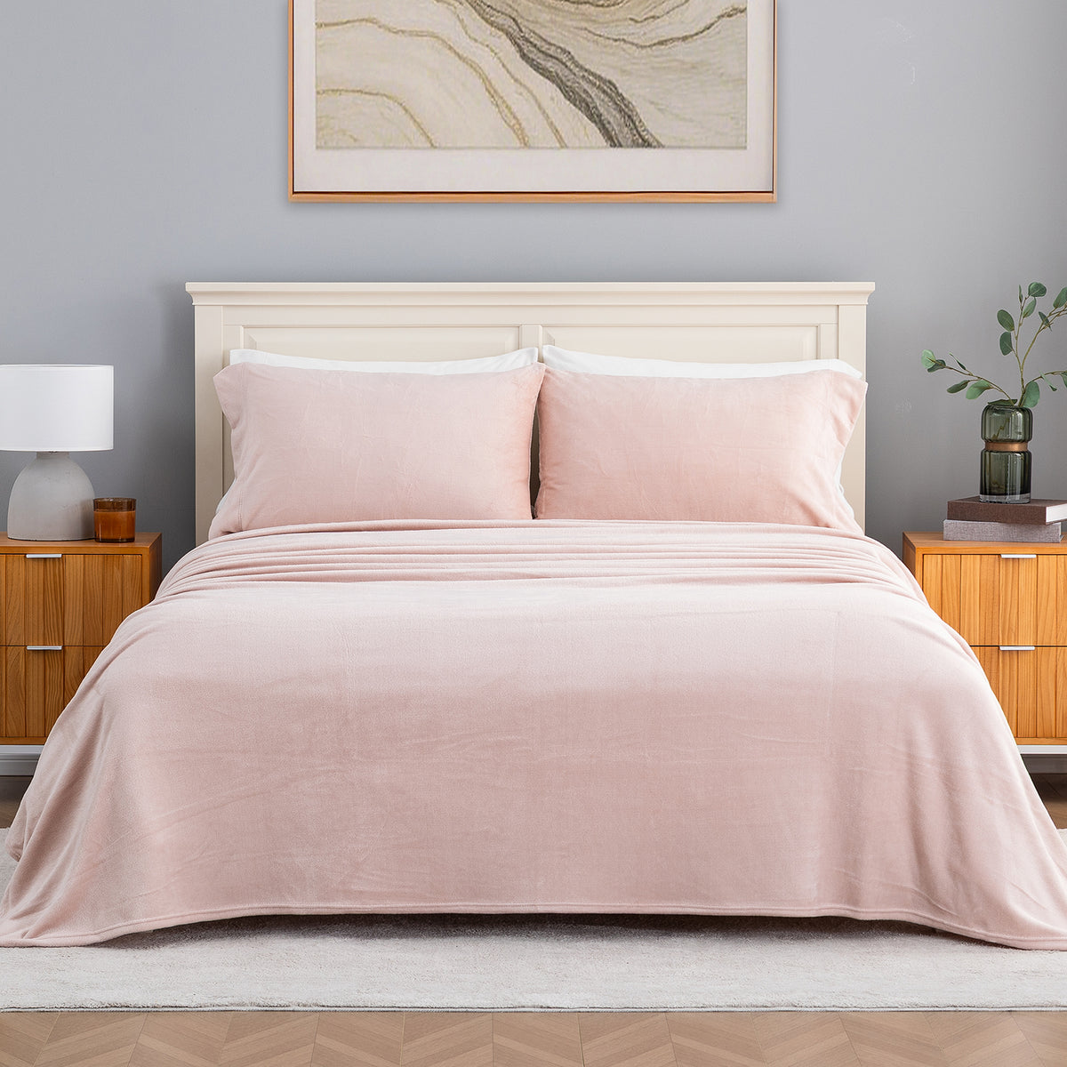 A neatly made bed in a styled bedroom setting, featuring light pink bedding including a duvet cover and two matching pillows, set against a gray wall with a white headboard, wooden nightstands, and a framed print.
