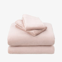 A stack of three folded plush bedding pieces, likely a blanket, pillowcase, and pillow sham, in a soft dusty pink color, set against a plain white background.