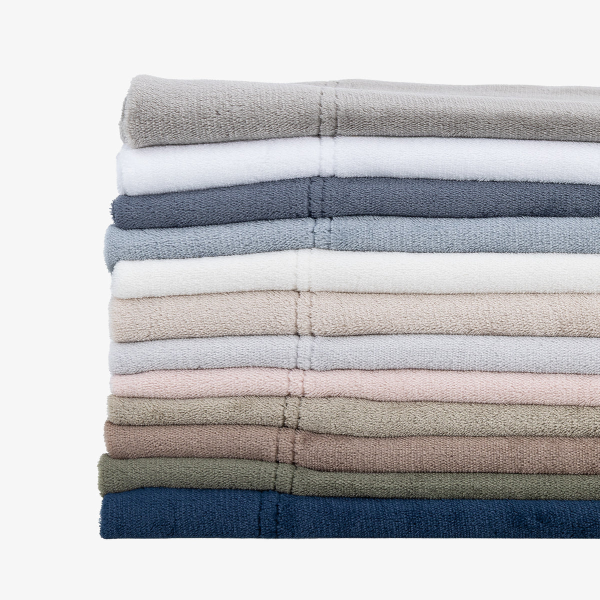 A stack of folded cotton towels in various muted colors, including gray, white, blue, beige, pink, brown, and navy, arranged vertically on a clean white background.