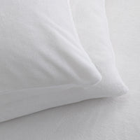 A close-up of a white pillowcase resting on a white textured sheet, showing the soft fabric texture and clean bedding presentation.
