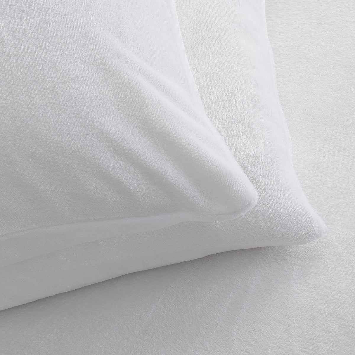 A close-up of a white pillowcase resting on a white textured sheet, showing the soft fabric texture and clean bedding presentation.