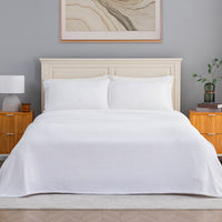 A neatly made bed with white bedding and two white pillows, set against a light gray wall with a cream headboard, wooden nightstands, a lamp, and framed wall art.