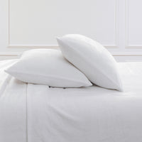 Two white pillows resting on white bedding against a white paneled wall.