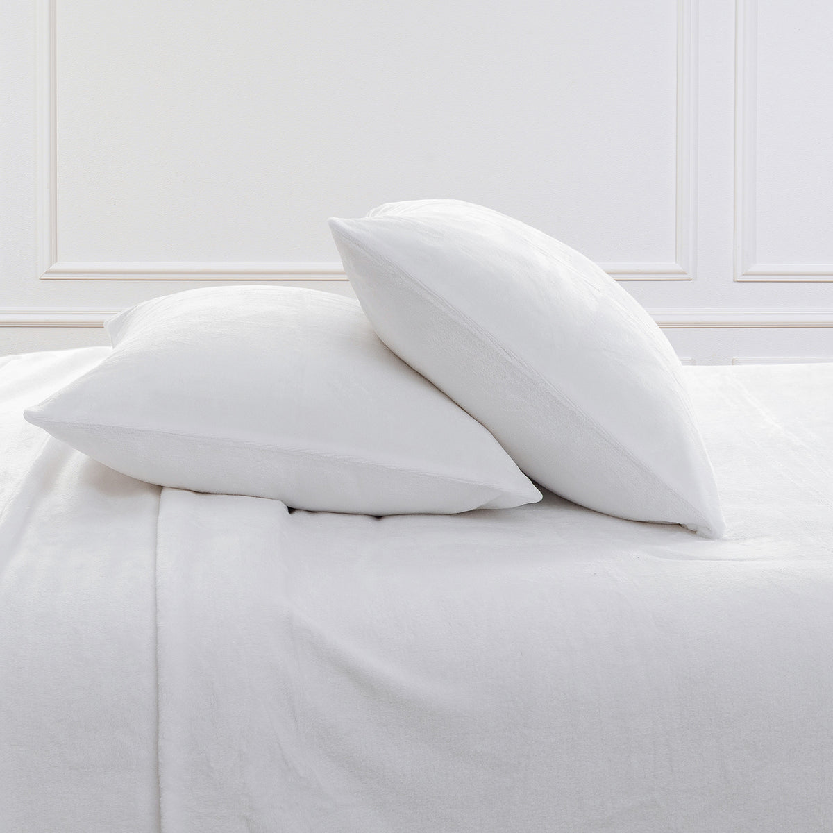 Two white pillows resting on white bedding against a white paneled wall.