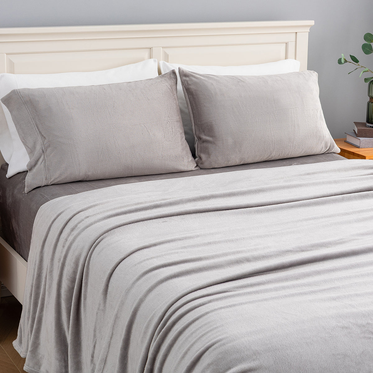 A neatly made bed with a light gray blanket, two matching gray pillowcases, white pillows, and a cream-colored wooden headboard in a bedroom setting.