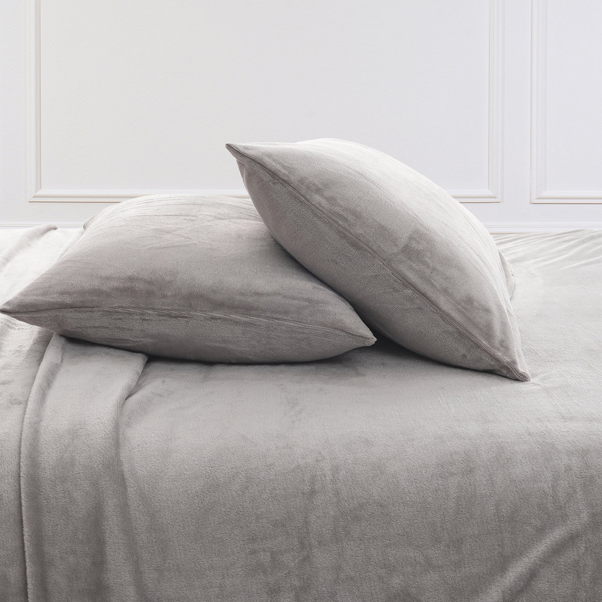 Two light gray plush pillows resting on a matching gray bedspread against a white paneled wall.