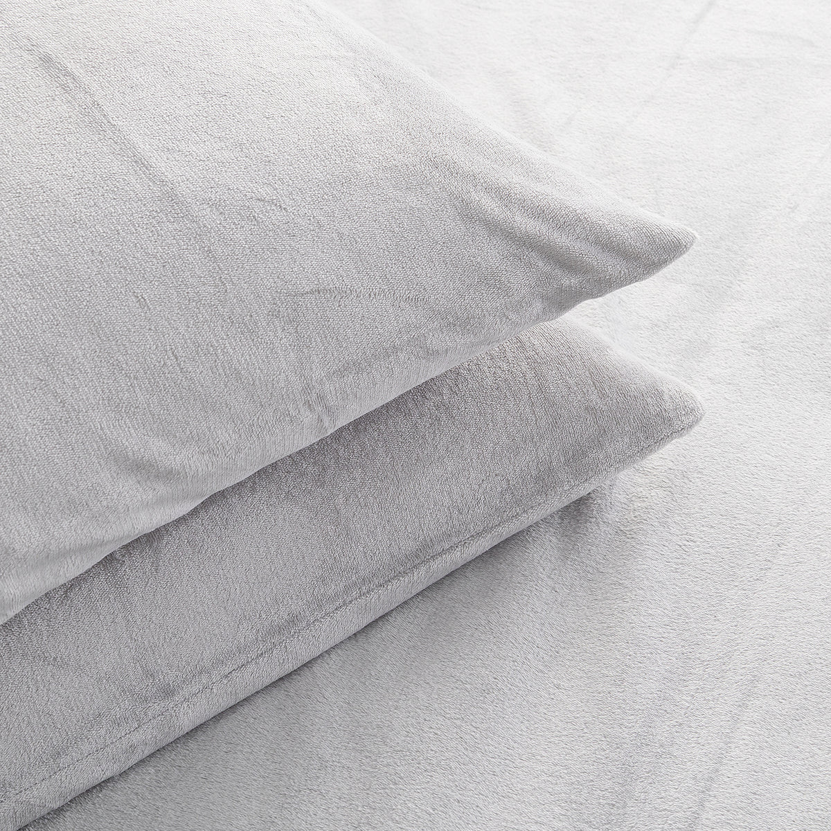 Two light gray plush pillows resting on a matching gray textured bedsheet.