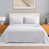 A neatly made bed with a light gray sheet and two matching pillows, styled in a bedroom with a cream headboard, wooden nightstands, a lamp, and framed wall art.