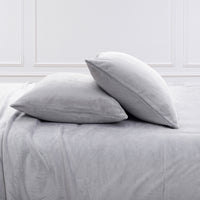 Two light gray pillowcases resting on a matching gray bedsheet in a bedroom setting with white paneled walls.