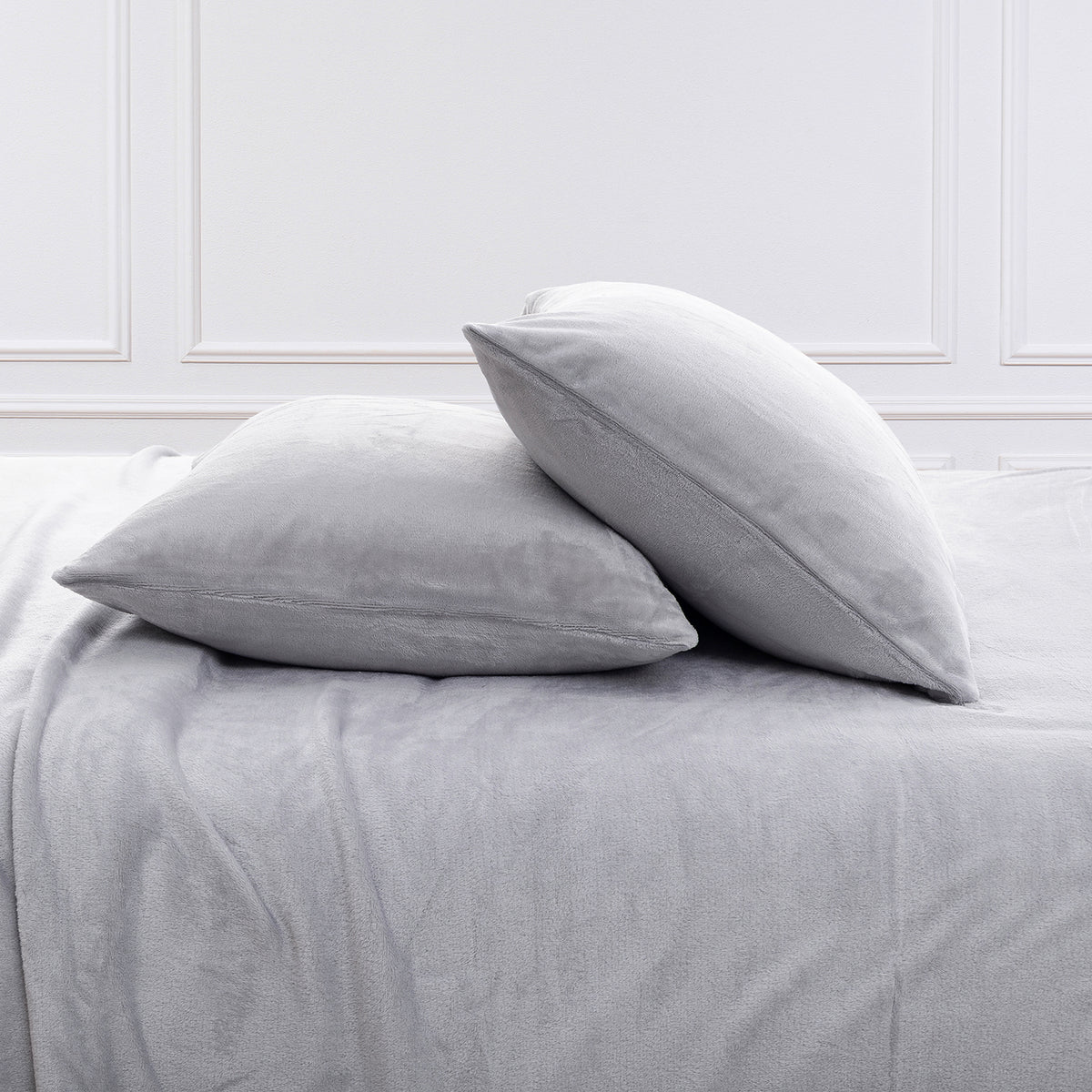 Two light gray pillowcases resting on a matching gray bedsheet in a bedroom setting with white paneled walls.