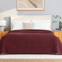 A Polartec Microfleece Blanket in deep fig draped over a bed in a bright bedroom.