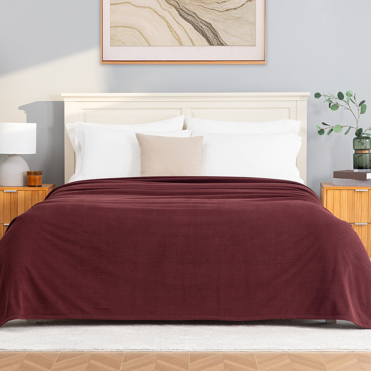 A Polartec Microfleece Blanket in deep fig draped over a bed in a bright bedroom.