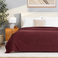 A Polartec Microfleece Blanket in deep fig draped over a bed in a bright bedroom.