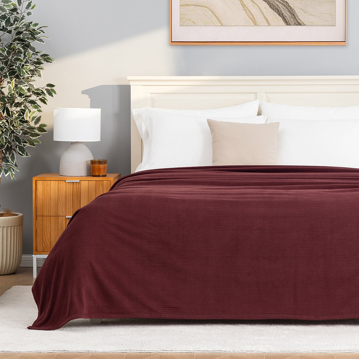A Polartec Microfleece Blanket in deep fig draped over a bed in a bright bedroom.