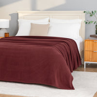 A Polartec Microfleece Blanket in deep fig draped over a bed in a bright bedroom.