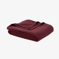A Polartec Microfleece Blanket in deep fig folded neatly on a white surface.