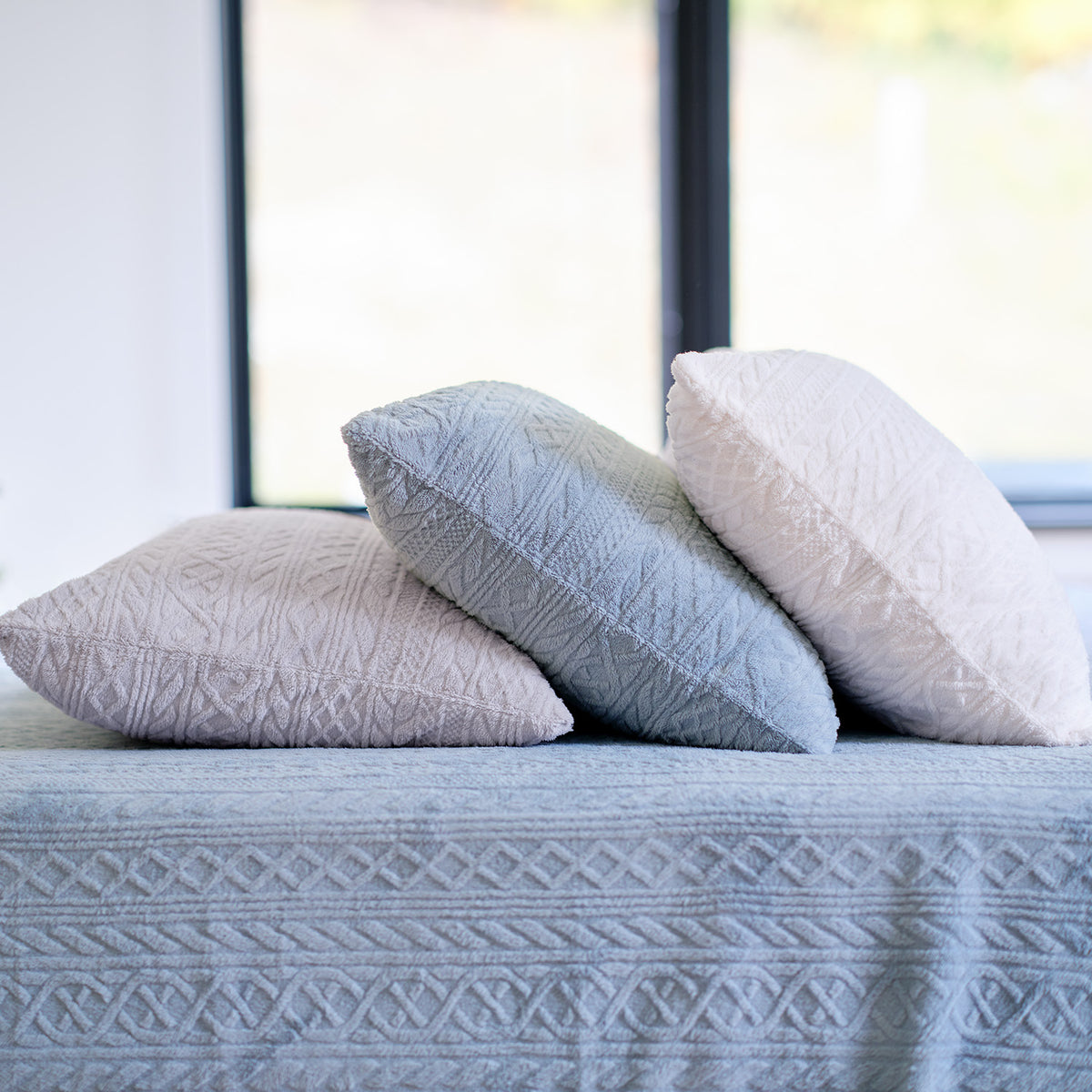 Three textured VelvetLoft® Plush pillowcases in grey, blue and cream on a bed made in Textured Polar Blue