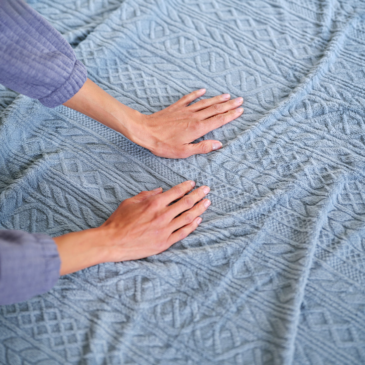Hands smoothing the VelvetLoft® Plush Sheet Set in Textured Polar Blue, showing its raised cable pattern