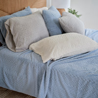 VelvetLoft® Plush Sheet Set in Textured Polar Blue on a bed with a rattan headboard, styled with textured pillowcases in grey, blue and cream