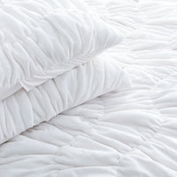 A white ruched VelvetLoft Comforter Set decorated on a bed in a bright room.
