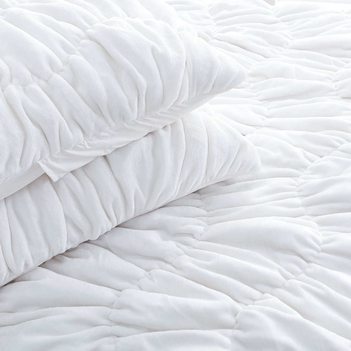 A white ruched VelvetLoft Comforter Set decorated on a bed in a bright room.