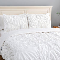 A white ruched VelvetLoft Comforter Set decorated on a bed in a bright room.