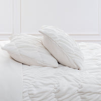 A white ruched VelvetLoft Comforter Set decorated on a bed in a bright room.