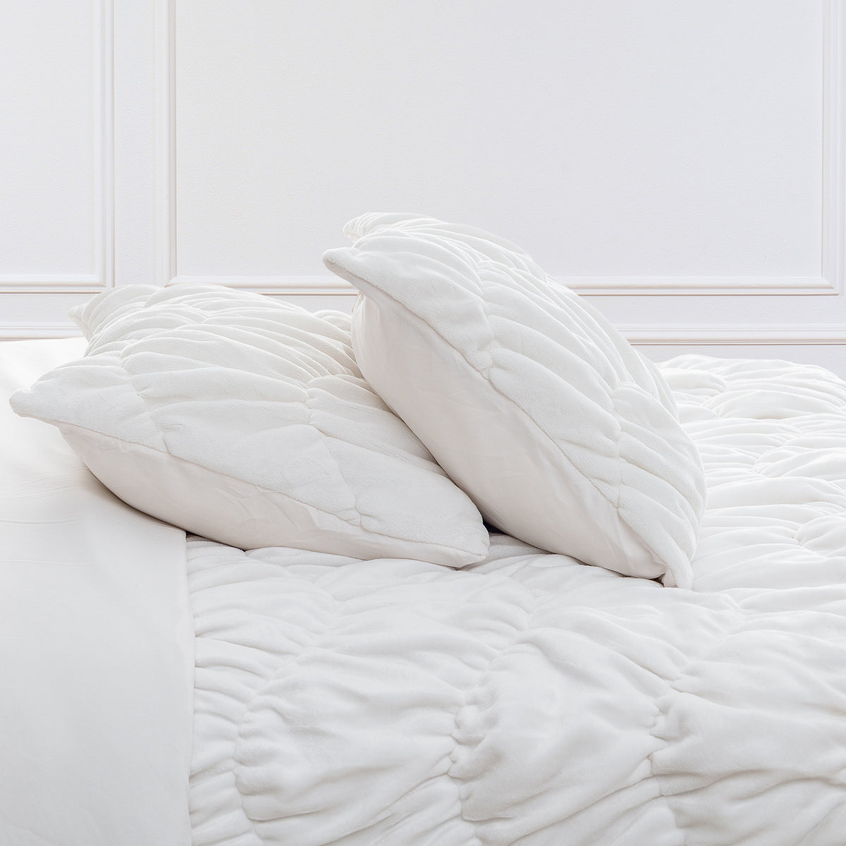 A white ruched VelvetLoft Comforter Set decorated on a bed in a bright room.