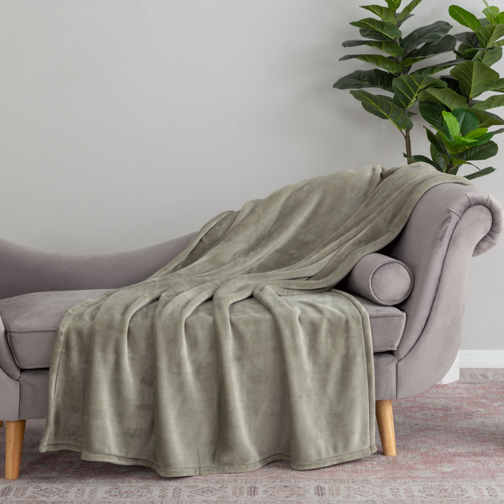 Green blanket draped over a gray sofa with a plant in the background