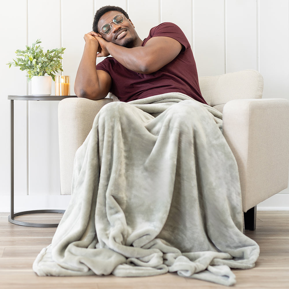 Man sitting on a couch with a green blanket draped over him in a cozy living room.