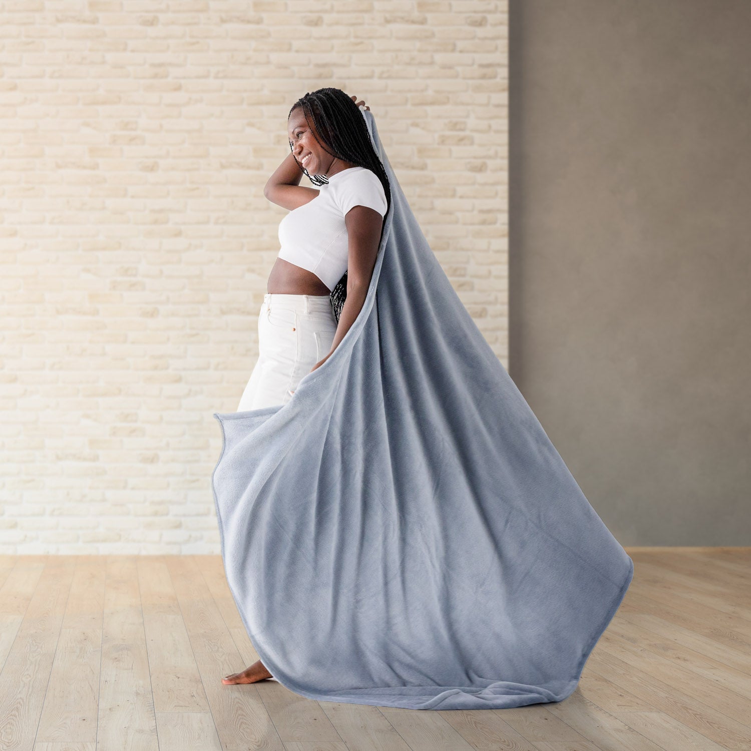 Woman holding a blue throw blanket in a room with a wooden floor and light-colored walls.