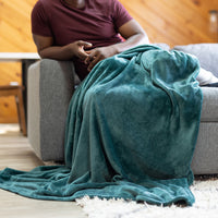 Person sitting on a couch with a teal blanket draped over them in a cozy living room.