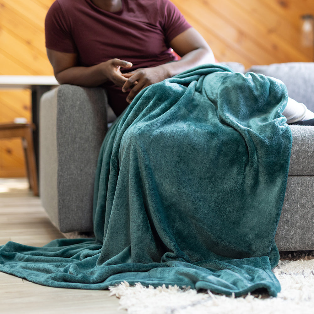 Person sitting on a couch with a teal blanket draped over them in a cozy living room.