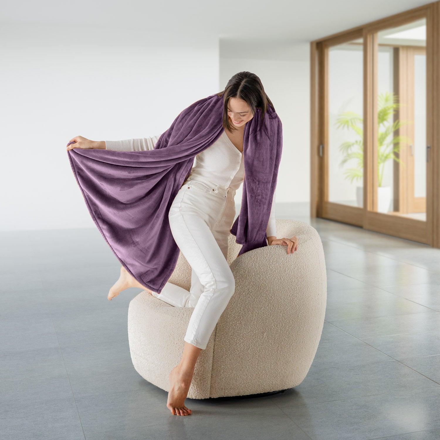 Woman sitting on a beige ottoman holding a purple throw blanket in a modern room.